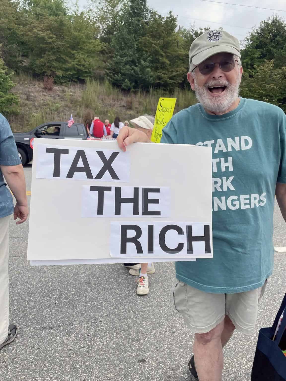 Man holding a sign that says 'Tax the Rich' at a protest in Haywood.