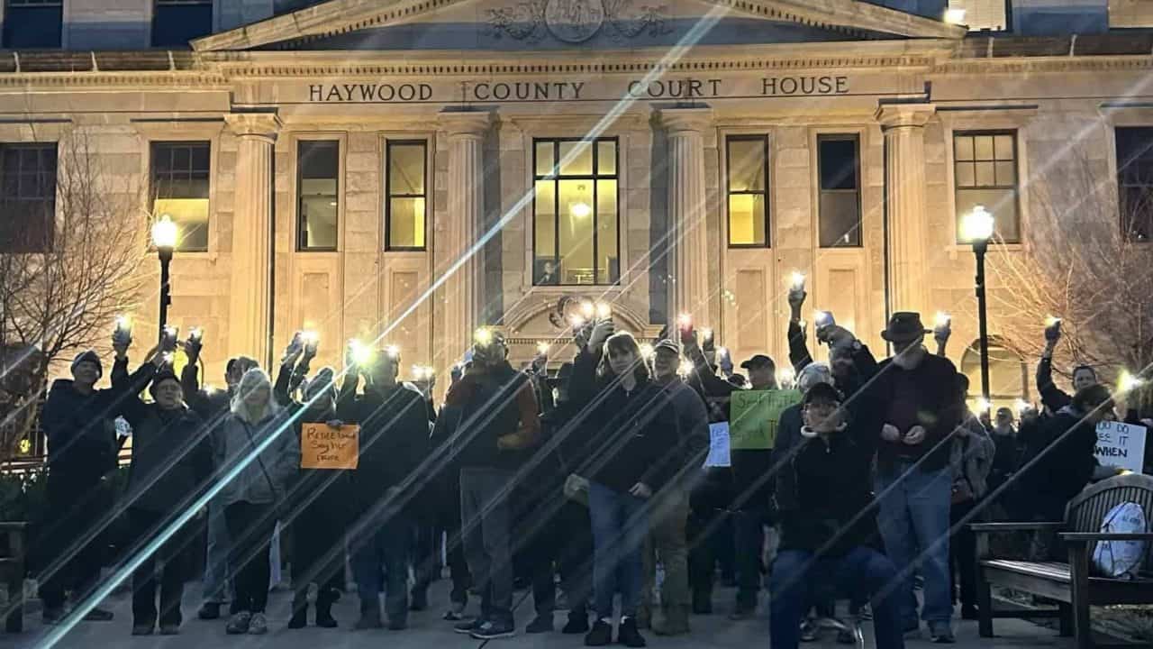 People protesting outside Haywood County Courthouse at night with signs and raised fists.