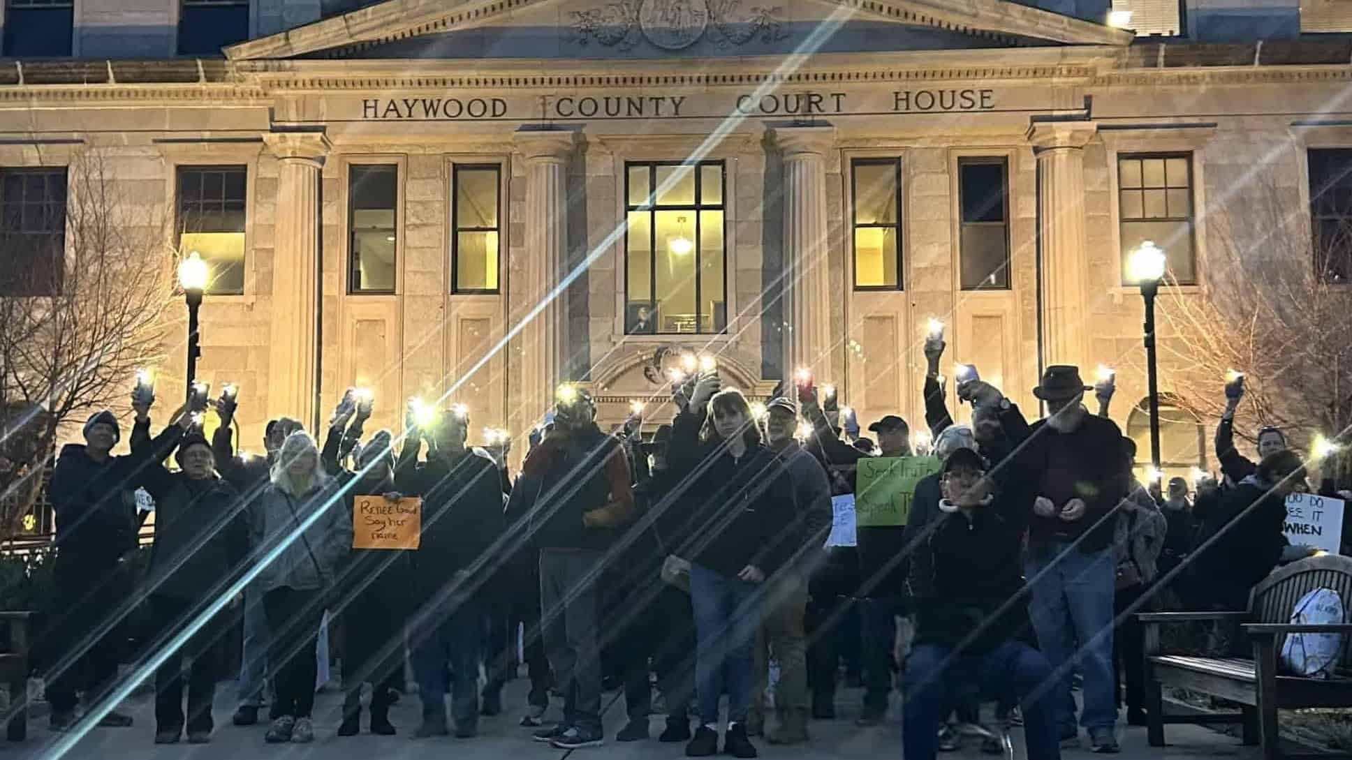 People protesting outside Haywood County Courthouse at night with signs and raised fists.